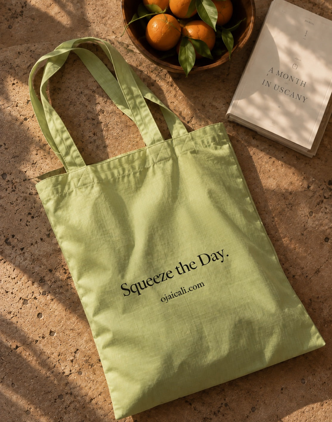 The green market tote flat on stone with a bowl of pixie tangerines